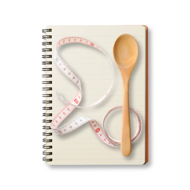 Overhead shot of spiral notebook with measuring tape and wooden spoon, on white background with clipping path. Diet concepts.