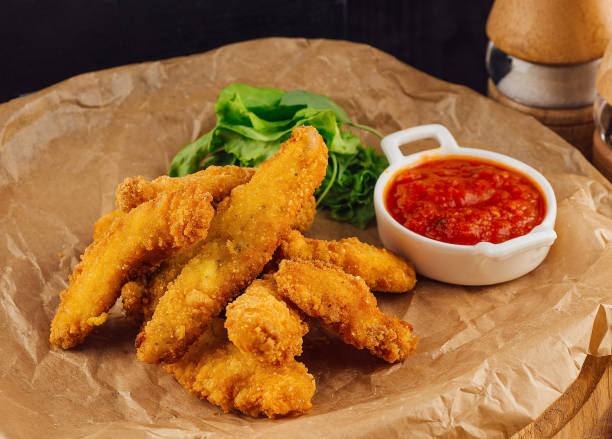 istock Breaded chicken strips lying on baking paper with spices around 2172774592