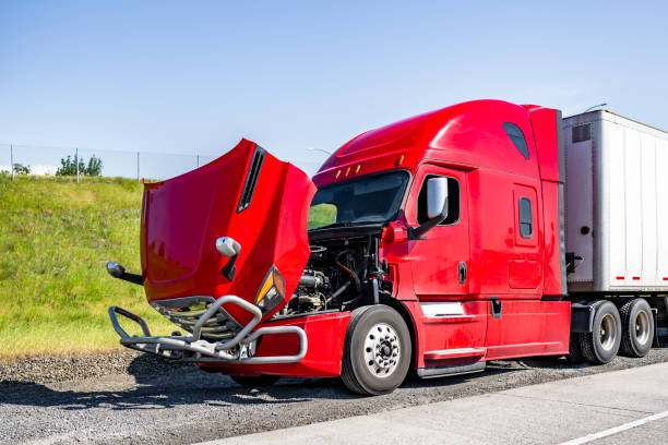 Broken red big rig semi truck with open hood and dry van semi trailer standing out of service on the road shoulder waiting for the towing truck or mobile road assistant for engine repair help stock photo