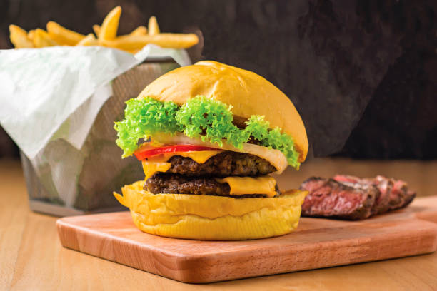 Double Beef Cheeseburger with Lettuce, Jalapeno, Tomato, Cheese, Steak Slices isolated on wooden board with french fries basket side view of fastfood