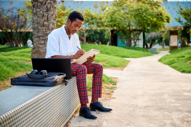 istock A young Black man sits on a bench in an urban area, sketching ideas in a notebook while his laptop and bag sit nearby 2172805063