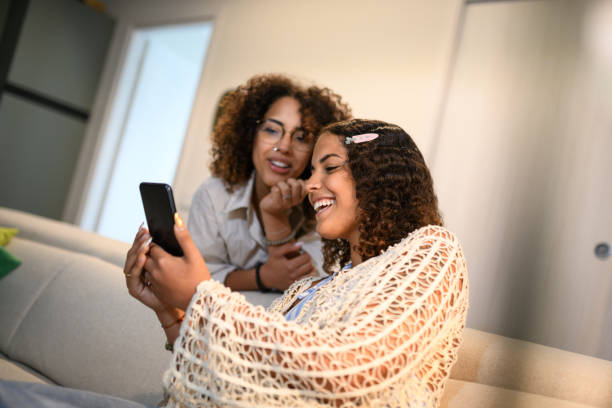 istock Sisters relaxing on the sofa with smartphone 2172816693
