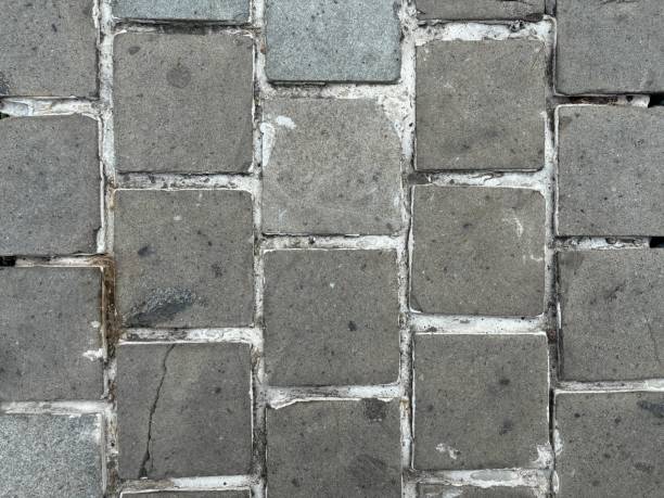istock Close-up of square paving stones with visible wear and cracks, arranged in a grid pattern. 2172817264