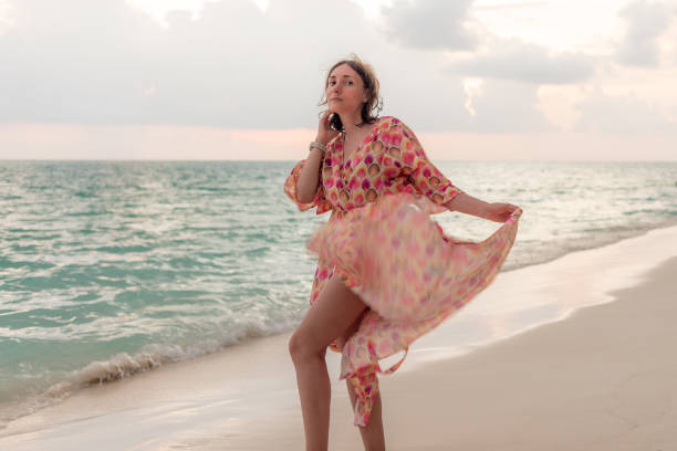 Woman in a long flowy dress walking down tropical beach at sunset
