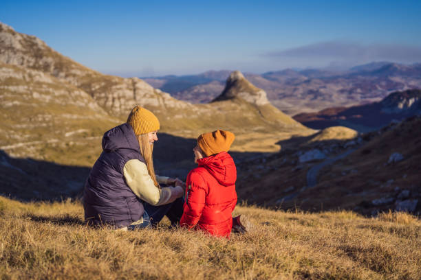 Montenegro. Mom and son tourists in the background of Durmitor National Park. Saddle Pass. Alpine meadows. Mountain landscape. Travel around Montenegro concept Montenegro. Mom and son tourists in the background of Durmitor National Park. Saddle Pass. Alpine meadows. Mountain landscape. Travel around Montenegro concept. stone bench top view stock pictures, royalty-free photos & images
