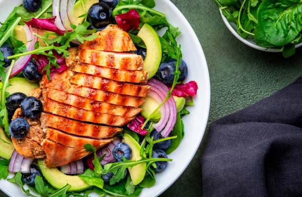 istock Green salad with grilled chicken, avocado and blueberries, rustic background, top view 2172860254