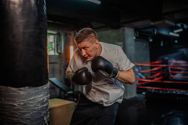 istock Boxer in grey shirt leans forward, targeting heavy bag. 2172864302
