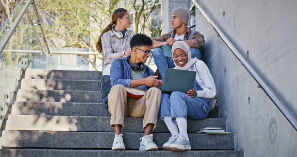 istock Group, education and learning on campus, laptop and collaboration for research and communication with friends. Happy, online and outdoor at college, students and people with smile, stairs or backpack 2172873355