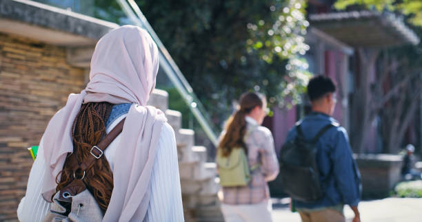 istock University, students and woman in hijab walking from back with diversity, backpack and study in education. Culture, equality and Muslim college girl on campus for morning commute to school with group 2172873370