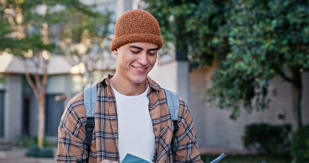 istock University, student and man reading outdoor on campus with book for education, learning and scholarship. Gen z, person and happy at college for studying, knowledge and backpack for research 2172873495