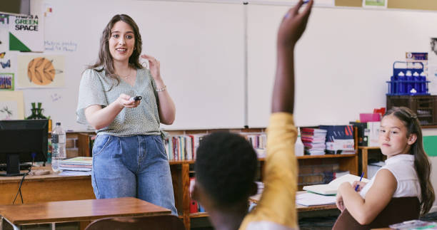 istock Smiling, intelligent and happy teacher points at a student who has a question in an educational classroom. A young black scholar with an arm raised ready to answer in a primary school classroom 2172874620