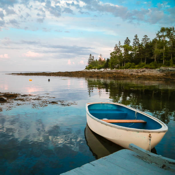 A blue boat docked at shore and blue sky reflection on the water at Hancock Point, Maine.