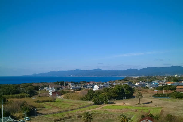 A picturesque view of a seaside village with the vast blue ocean stretching towards distant mountains. The clear sky and peaceful coastal scenery create a serene and inviting atmosphere.
