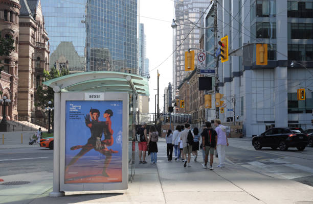 Queen Street West at Bay Street, Toronto, Canada Toronto, Canada - August 25, 2024: Pedestrians walk east past a bus shelter poster on Queen Street West. Summer morning near the romanesque Toronto Old City Hall in the downtown district. bus shelter stock pictures, royalty-free photos & images