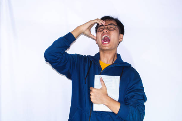 a teenager wearing a dark blue jacket and glasses, is furious while holding a book