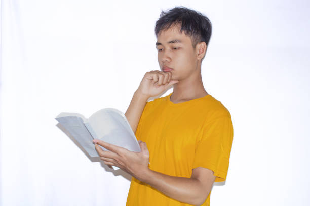 Asian teenager wearing a yellow t-shirt, holding a book with a focused expression