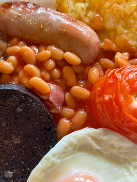 Stock photo showing close-up, elevated view of a white plate containing a Full English breakfast with a bacon rasher, a grilled sausage, a pile of baked beans, a sunny-side-up fried egg, a cooked tomato, a hash brown and a slice of black pudding
* Not AI modified * imagen de fotograma completo de desayuno inglés frito completo de tocino rasher, salchicha a la parrilla, pila de frijoles horneados, huevo frito con el lado soleado hacia arriba, tomate cocido, papas fritas y rodaja de morcilla, vista elevada