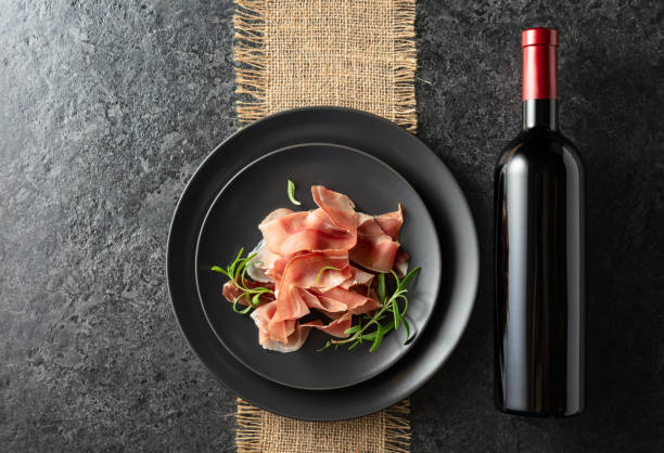 istock Bottle of red wine and prosciutto on a black plate. 2172919424