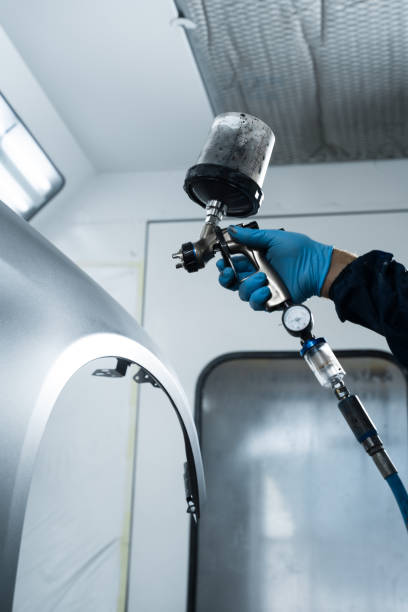 istock Mechanic from vehicle maintenance service is spreading paint on car using dark spray and paint gun. Professional worker wearing protective gloves is painting automobile. 2172922460