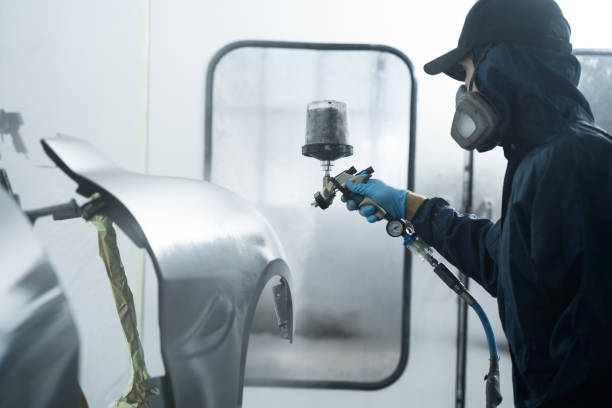 istock Car painter is changing the color of vehicle using sponge and paint sprayer. Worker is painting car in dark color with HVLP spray gun. 2172922720