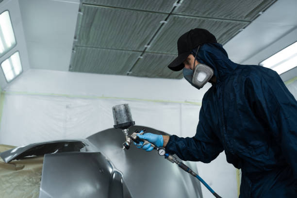 istock Car painter is changing the color of vehicle using sponge and paint sprayer. Worker is painting car in dark color with HVLP spray gun. 2172922744