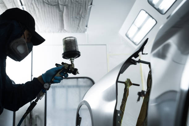 istock Car painter is changing the color of vehicle using sponge and paint sprayer. Worker is painting car in dark color with HVLP spray gun. 2172922746
