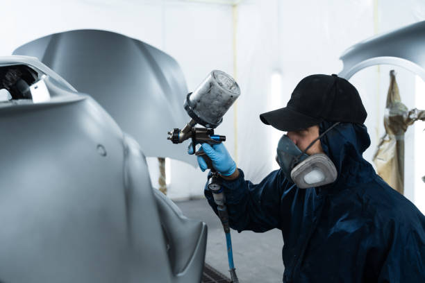 istock Mechanic from vehicle maintenance service is spreading paint on car using dark spray and paint gun. Professional worker wearing protective gloves is painting automobile. 2172922897