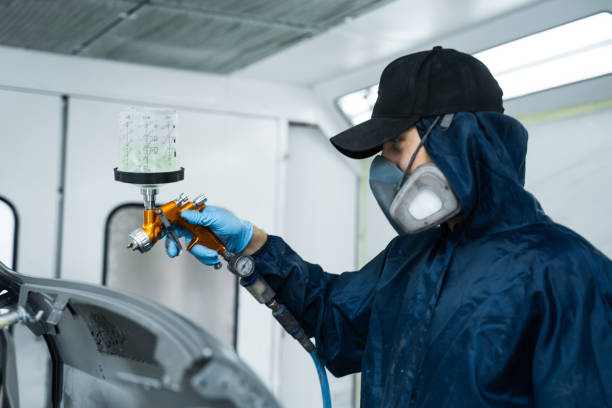 istock Car painter is applying lacquer on car using LVLP spray gun. Putting lacquer on metal to give surface smooth appearance. 2172923380