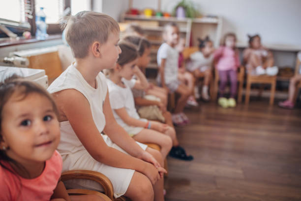 A Back view of child group sitting on floor looking at wall