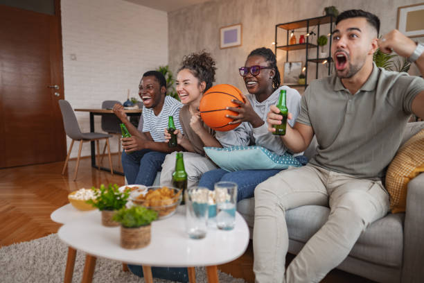 istock Friends enjoying a lively evening watching sports on TV while sharing snacks and drinks in a cozy living room 2172931252
