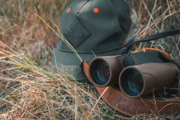 Outdoor gear featuring binoculars and a green cap lying in dry grass, symbolizing a nature hike, camping, or hunting scene, perfect for themes of exploration, adventure, or wildlife observation.