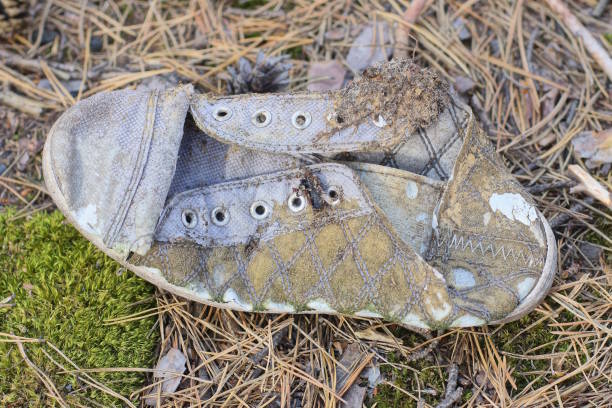 Low angle image depicting a pair of hiking boots, caked in mud, left abandoned at the side of the road. Focus on the boots with the receding perspective of the road defocused beyond.