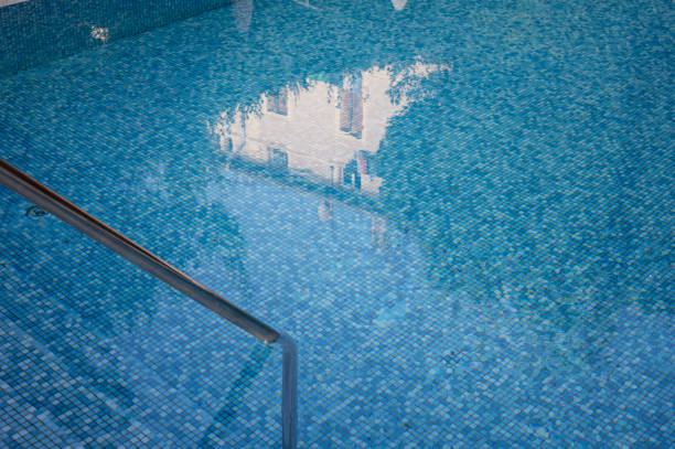 Swimming pool with stair and blue water. Grab bars ladder in the blue swimming pool. Ripple wave in pool for background and abstract. Summer relax concept. Texture of water surface. Space for text.