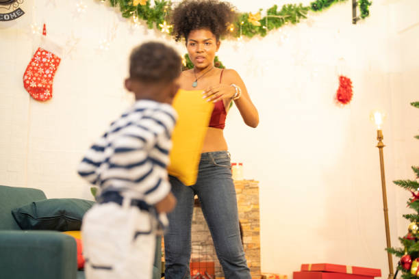 istock mother in a festive setting with a beautifully Christmas tree engages playfully with her child, who is lying on couch. The joyful atmosphere highlights holiday family bonding, home celebrations. 2172998921