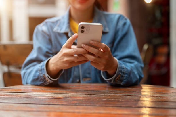 istock A cropped image of a woman in a denim jacket using smartphone while sitting at a table outdoors. 2173030913