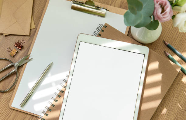 istock Stationery workspace with a blank tablet, notebook, and flowers on a wooden table, perfect for creative planning in natural light 2173045369