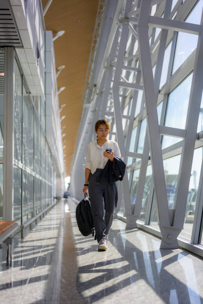 A beautiful Asian Chinese businesswoman walks along a pedestrian walkway at the airport during her business trip.