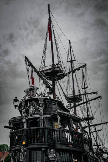 A small wooden boat with a white sail is on a black background. The boat is the main focus of the image, and it is a model or a toy. The black background emphasizes the boat's size