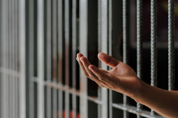 istock hands of a prisoner behind prison bars on black background 2173054591
