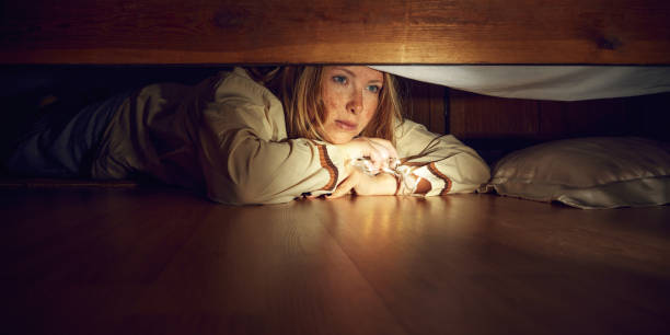 istock young woman lying under bed with pillow, feeling comfortable and safe. Nightmares, emotions of fear and stress. Hiding 2173057393