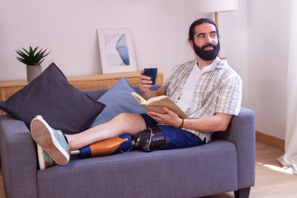 istock Young man with prosthetic leg relaxing on sofa, enjoying a book and coffee 2173064025