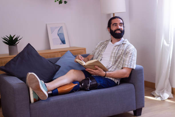 istock Smiling man with prosthetic leg reading a book on sofa at home 2173064061