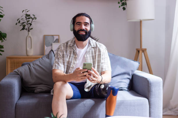 istock Smiling man with prosthetic leg using smartphone sitting on sofa at home listening music 2173064651
