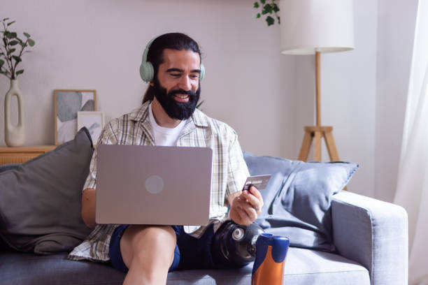istock Smiling man with prosthetic leg using laptop for online shopping at home 2173064670