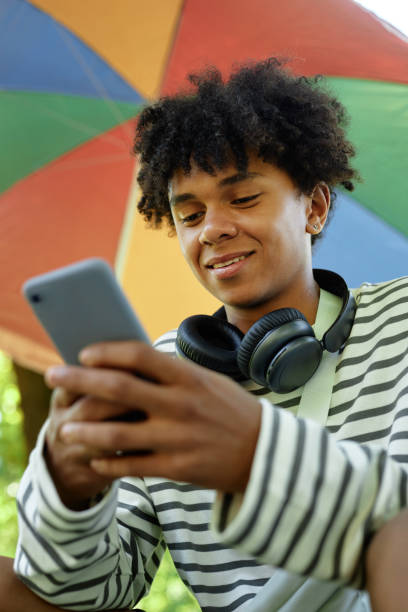 istock Smiling Black Boy with Headphones Using Phone Sitting in Park 2173069578