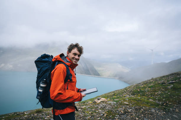 istock Backpacker uses digital tablet above alpine lake, smile at camera 2173072807