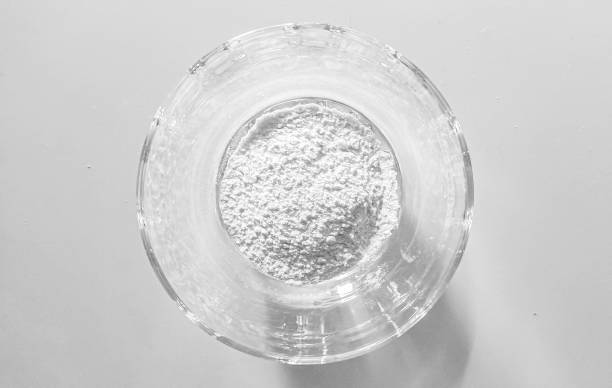 A transparent glass bowl on a white background contains a fine white powder, which could symbolize purity, simplicity, or minimalism, often used abstractly in arts and designs.