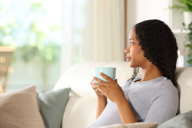 istock Black woman drinking coffee looking outside through a window 2173081864