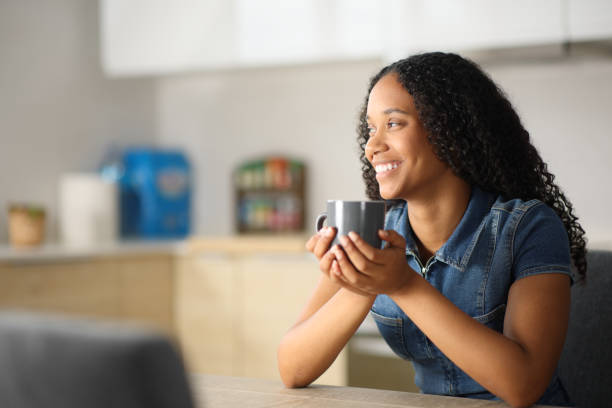 istock Happy black woman drinking coffee looking away in the kitchen 2173081936
