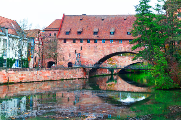Schlayerturm tower and Kettensteg Chain Bridge over Pegnitz river in Nuremberg, Bavaria Germany.  Bridge spans a river with a brick building in the background